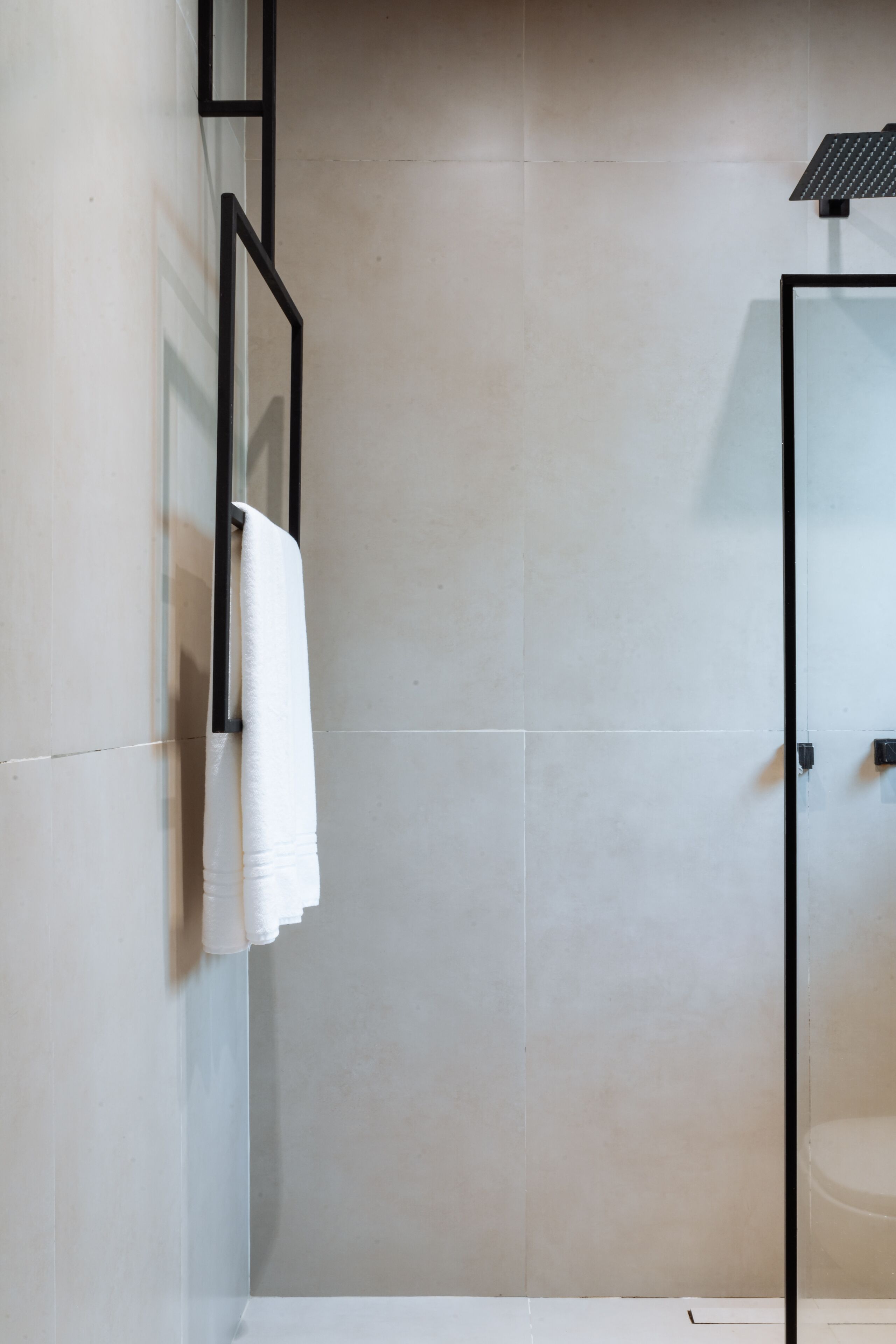 A modern bathroom with a glass shower enclosure, a white towel hanging on a metal towel rack, and a toilet.