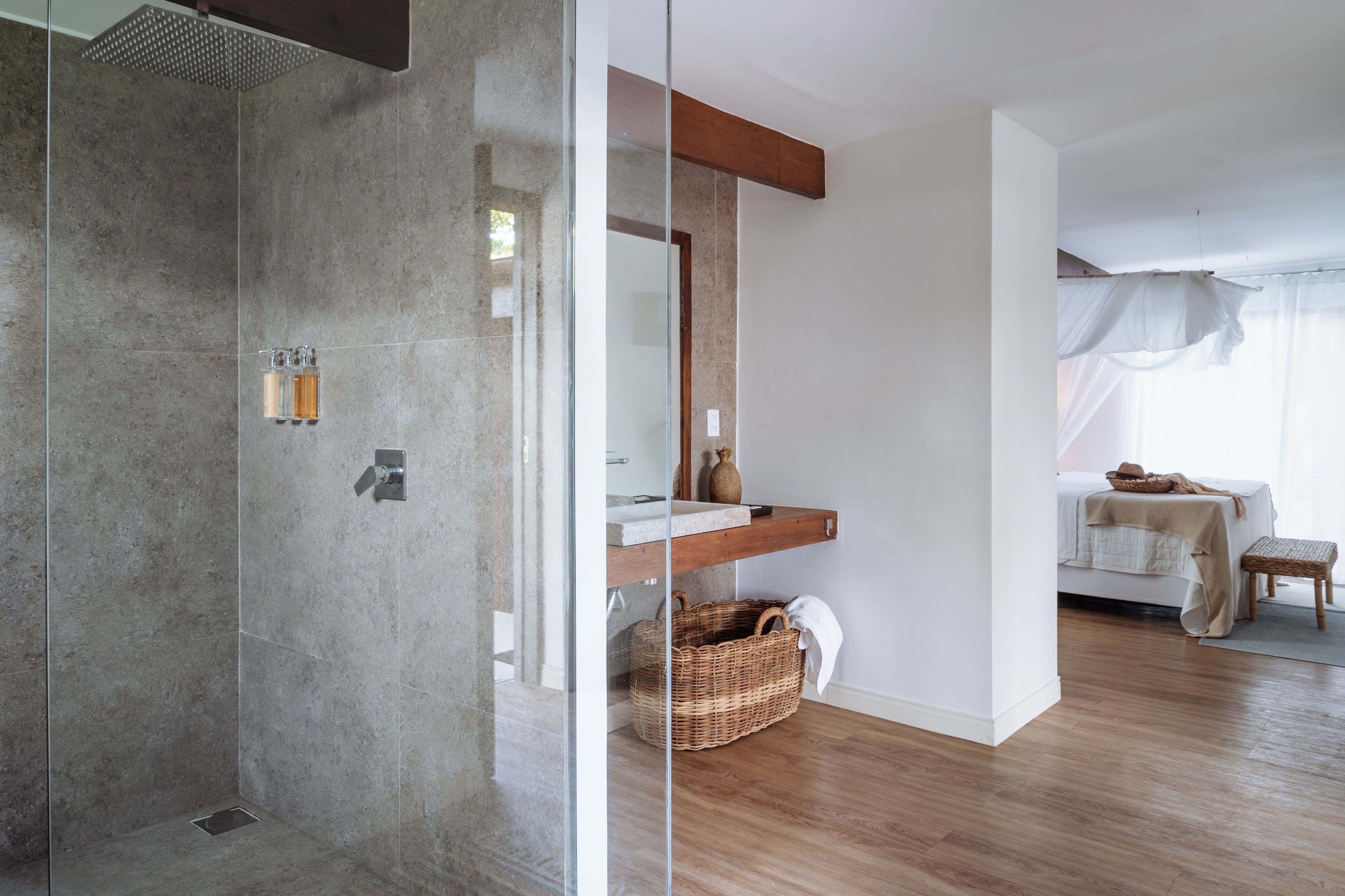 A modern bathroom with a glass shower enclosure, a wooden bench, and a wicker basket.