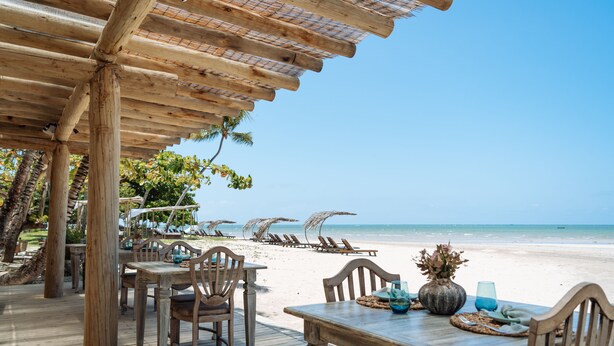 A wooden deck with tables and chairs, overlooking a beach with umbrellas and lounge chairs. - Vila dos Orixás Boutique Hotel (Cairu)