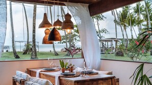 A wooden dining table with chairs, set for two, overlooking a beach with palm trees and the ocean. - Vila dos Orixás Boutique Hotel (Cairu)