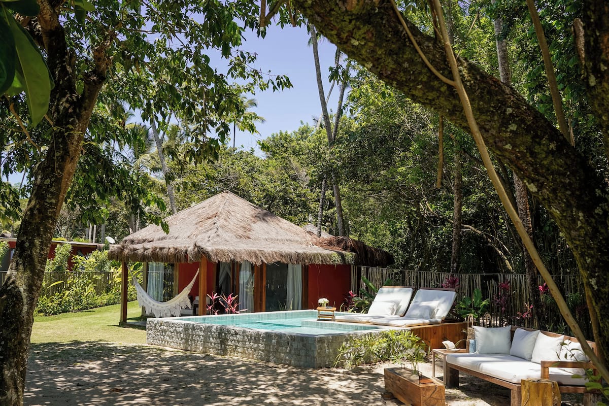 A pool area with a thatched-roof hut, lounge chairs, and a wooden bench.
