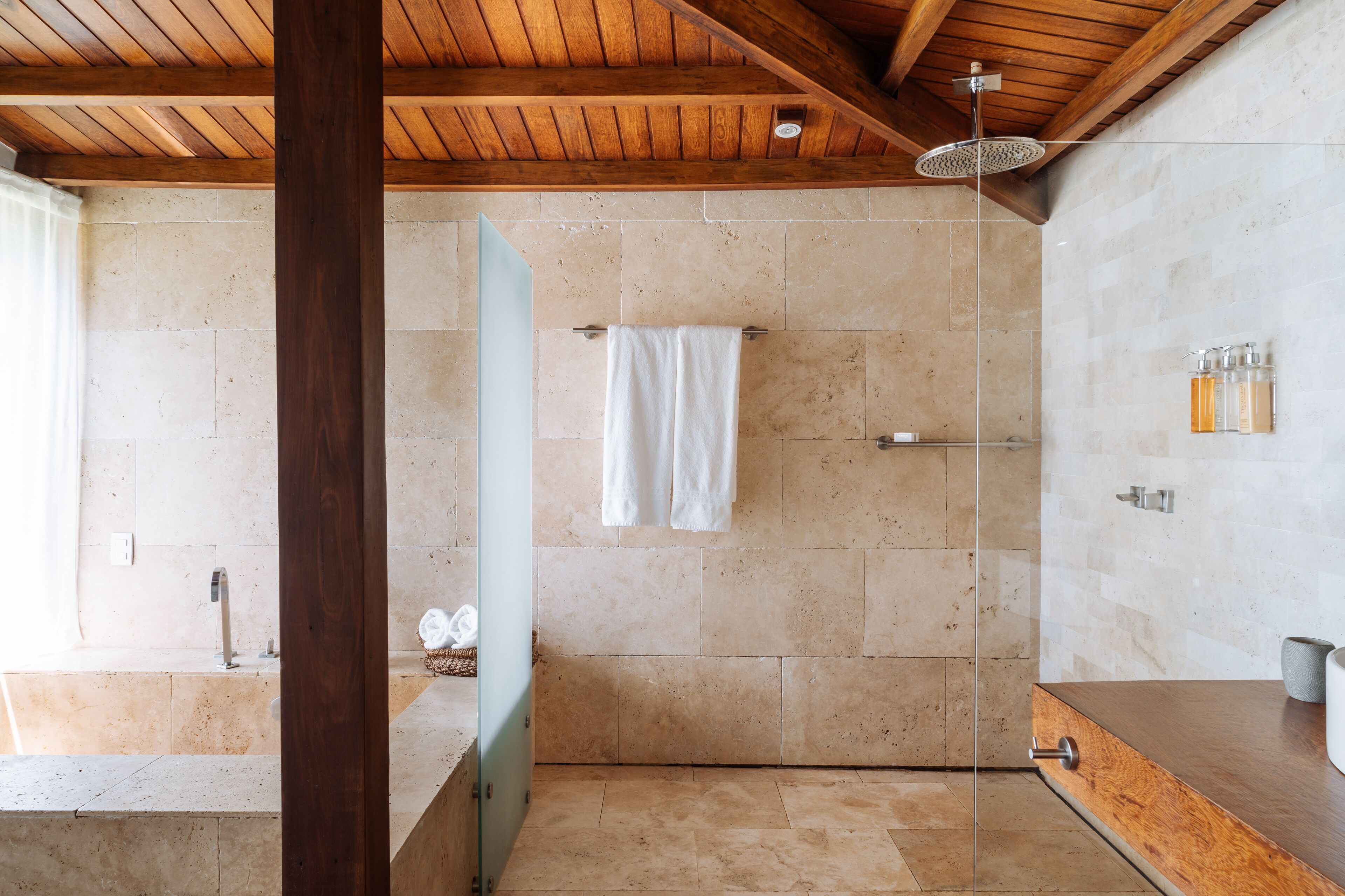 A modern bathroom with a shower, a wooden ceiling, and a stone wall.