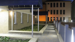 A pathway leading to a building with a blue awning and a brick wall. - Warsaw Apartments Magnolie (Warsaw)