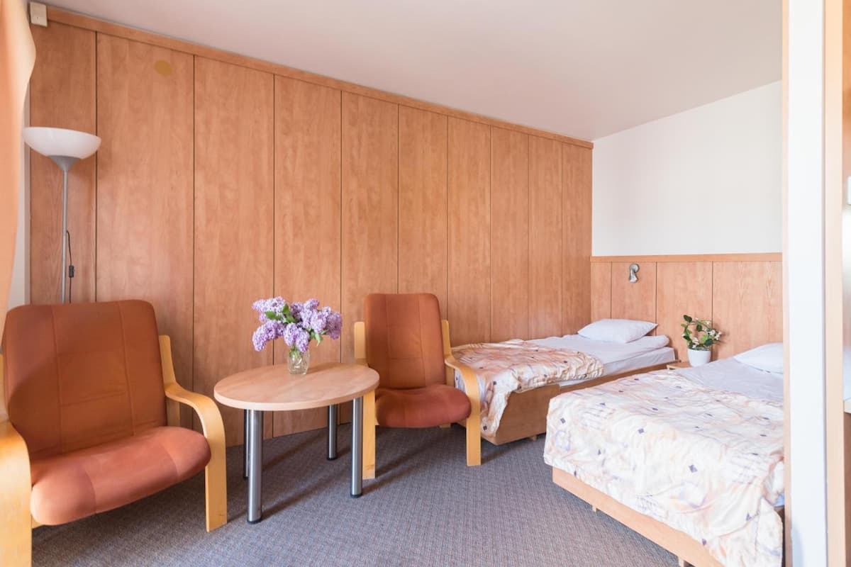 Ein Hotelzimmer mit zwei Einzelbetten, einem kleinen runden Tisch mit Blumenvase, zwei Sesseln und einer Lampe.