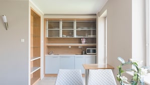 A compact kitchen with built-in cabinets, a microwave, and a kettle on the countertop. There is a dining area with a table and two chairs. - Warsaw Apartments Magnolie (Warsaw)