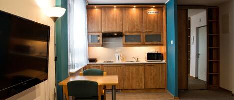 A compact kitchen with wooden cabinets, a microwave, and a sink. There is a dining area with a table and chairs.