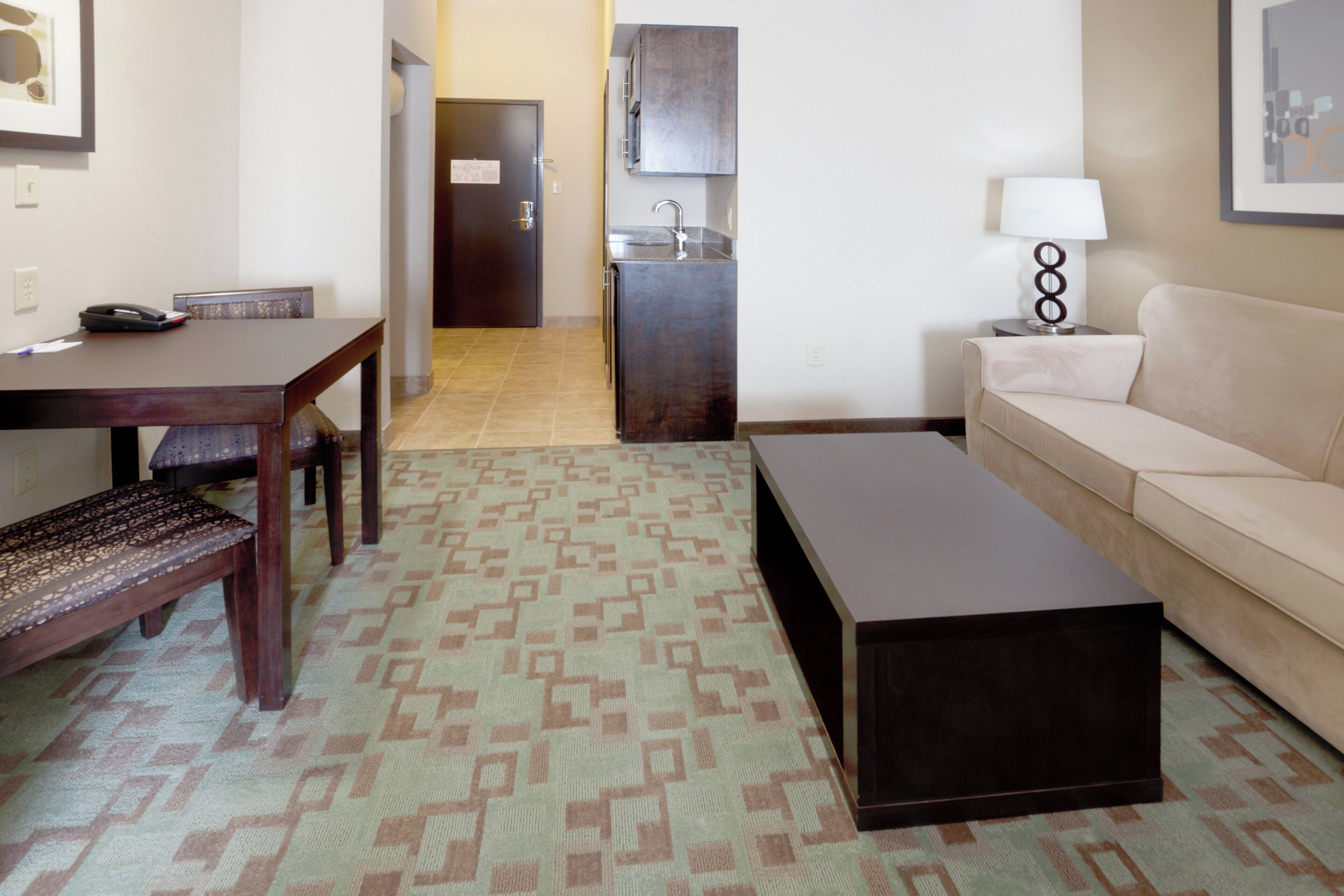 Una sala de estar con un sofá, una mesa de centro, una mesa de comedor con sillas y una alfombra estampada.