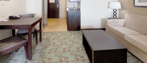 A living room with a sofa, a coffee table, a dining table with chairs, and a patterned rug.