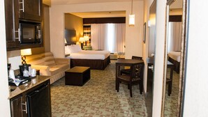 A hotel room with a bed, a sofa, a desk, a chair, a microwave, a coffee maker, and a small refrigerator.