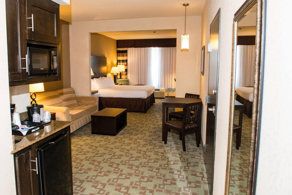 Habitación de hotel con cama, sofá, escritorio, silla, microondas, cafetera y refrigerador pequeño.