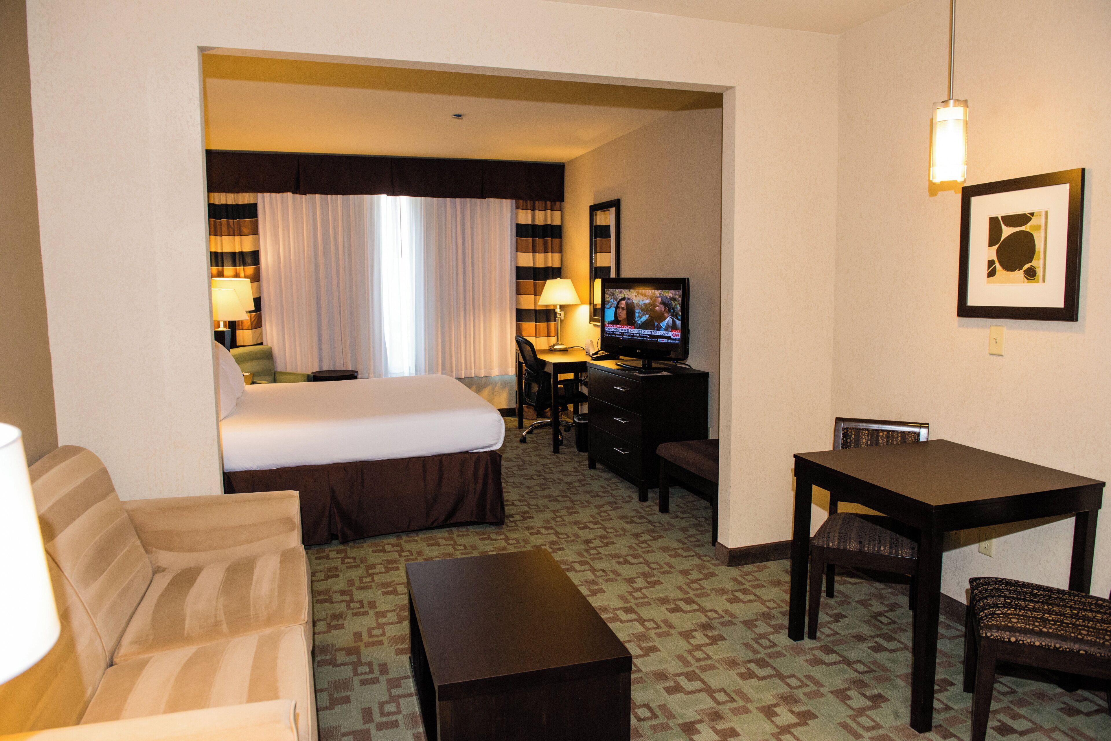 Habitación de hotel con cama, escritorio, silla, televisor y lámpara.