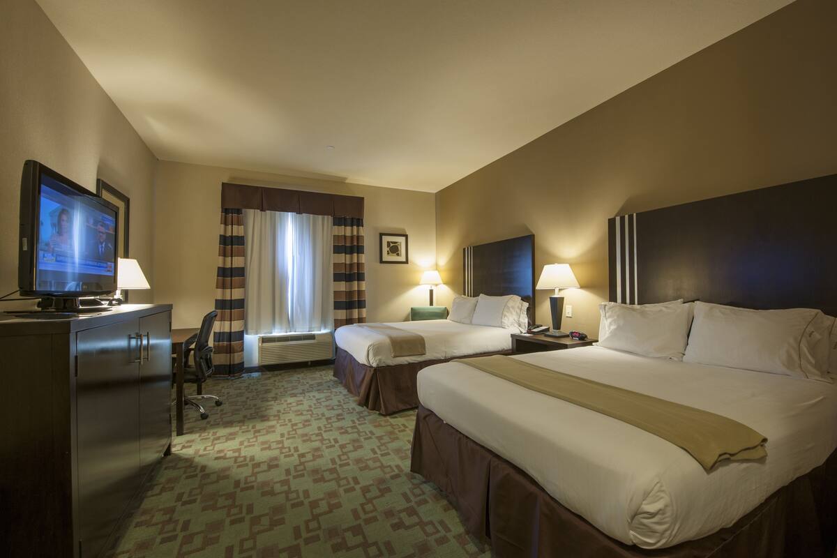 Habitación de hotel con dos camas, un escritorio con computadora, televisión y ventana con cortinas.