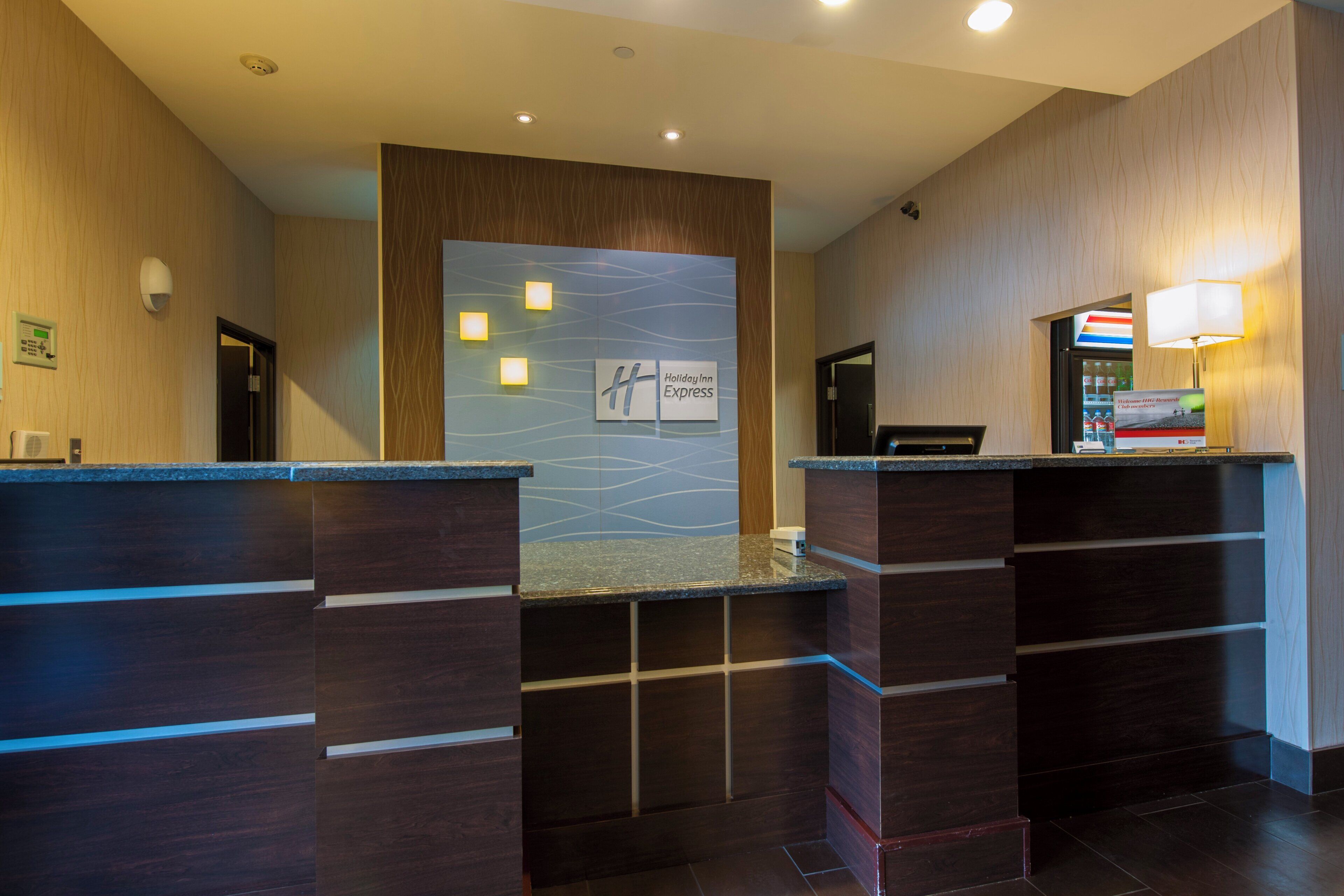 Un espace d’accueil avec une enseigne Holiday Inn Express, un comptoir de réception, un écran numérique et un distributeur automatique.