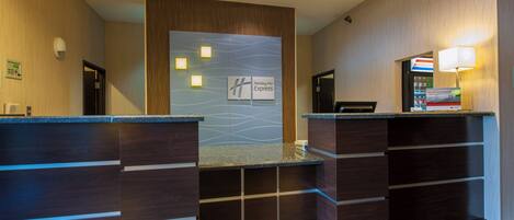 Un espace d’accueil avec une enseigne Holiday Inn Express, un comptoir de réception, un écran numérique et un distributeur automatique.