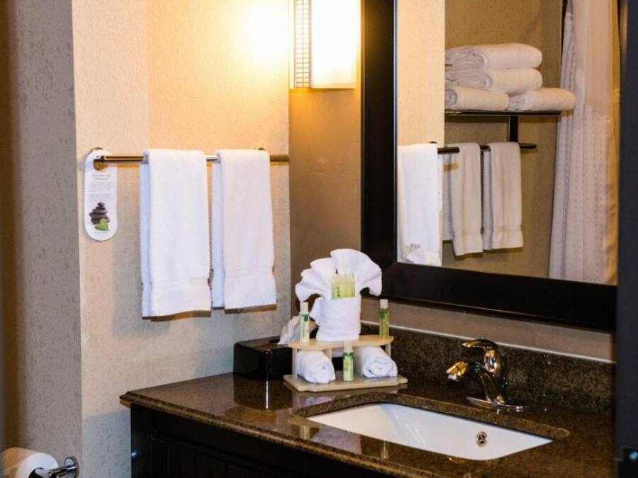 Un baño con lavamanos, espejo, toallero y artículos de aseo.