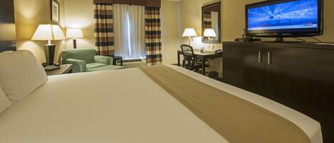 A hotel room with a large bed, a desk with a chair, a television, and a wardrobe.