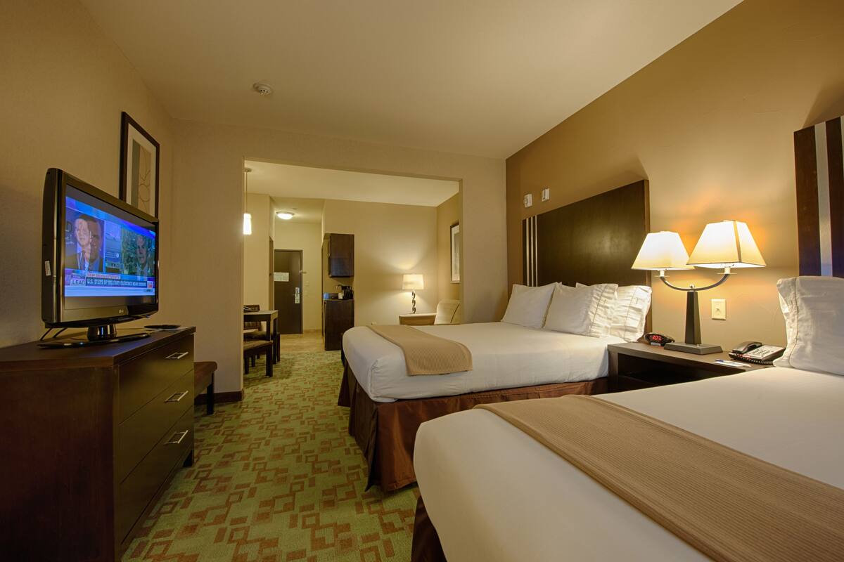 Habitación de hotel con dos camas, televisor, escritorio y lámpara.