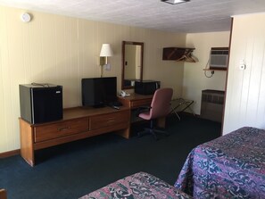 A hotel room with a wooden desk, a television, a telephone, a chair, a bed with patterned bedding, a mirror, and a coat rack. - Elmwood Motor Lodge (Boscawen)