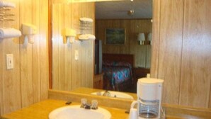 A bathroom with wooden paneling, a sink, a mirror, and a coffee maker. - Elmwood Motor Lodge (Boscawen)