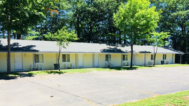 A row of motel rooms with individual doors, a parking lot, and a grassy area. - Elmwood Motor Lodge (Boscawen)