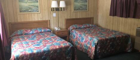 Une chambre avec deux lits, des murs lambrissés en bois, deux lampes fixées au mur et deux tableaux encadrés.