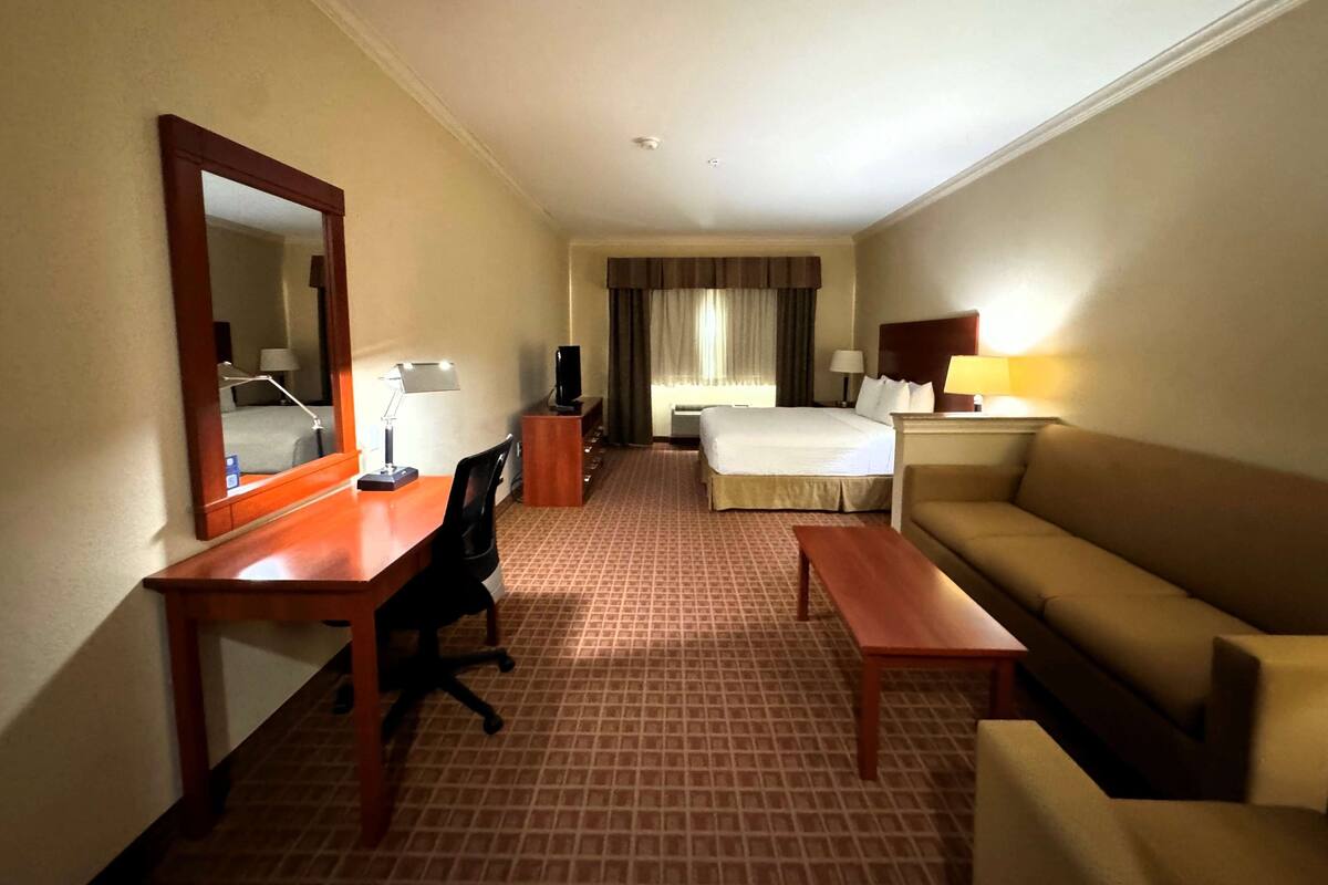 Une chambre d’hôtel comprenant un lit, un canapé, un bureau avec une chaise, un miroir et une lampe.