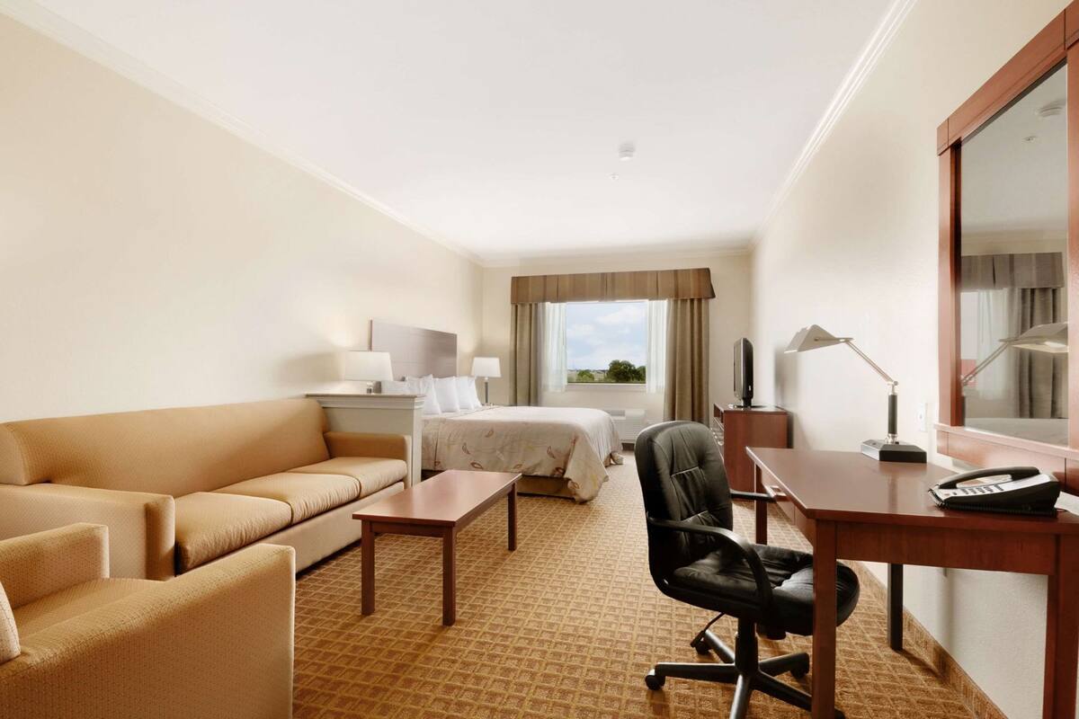 Une chambre d’hôtel avec un lit, un canapé, un bureau, une chaise, une télévision et une fenêtre donnant sur un paysage agréable.