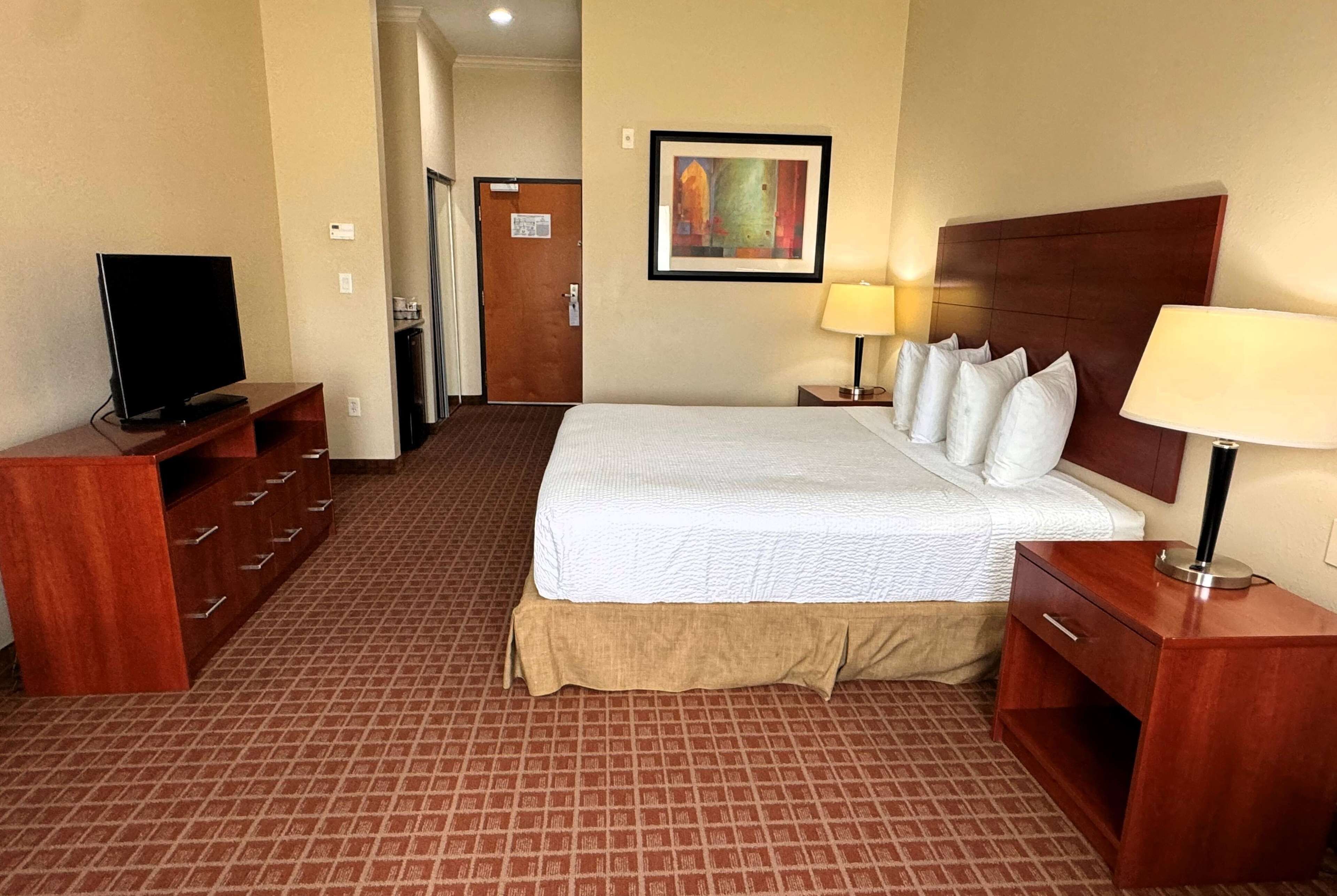 A hotel room with a large bed, a television, a desk, and a painting on the wall.