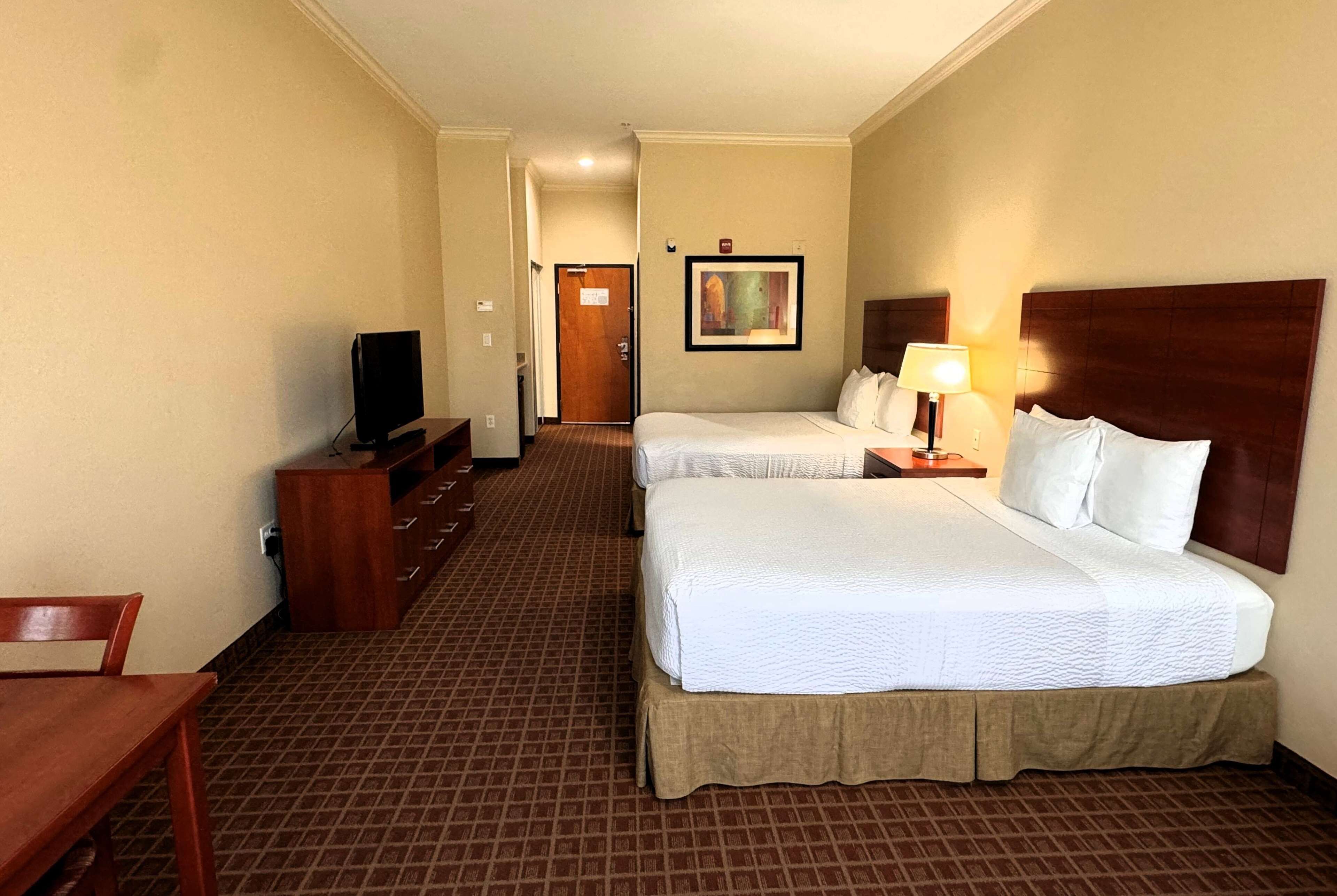 A hotel room with two beds, a television, a desk, and a painting on the wall.