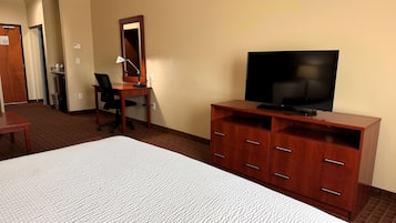 Une chambre d’hôtel avec un grand lit, un bureau en bois avec une chaise, un téléviseur posé sur un meuble en bois et un miroir au mur.