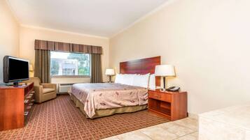 A hotel room with a bed, a TV, a desk, a chair, a lamp, and a telephone.