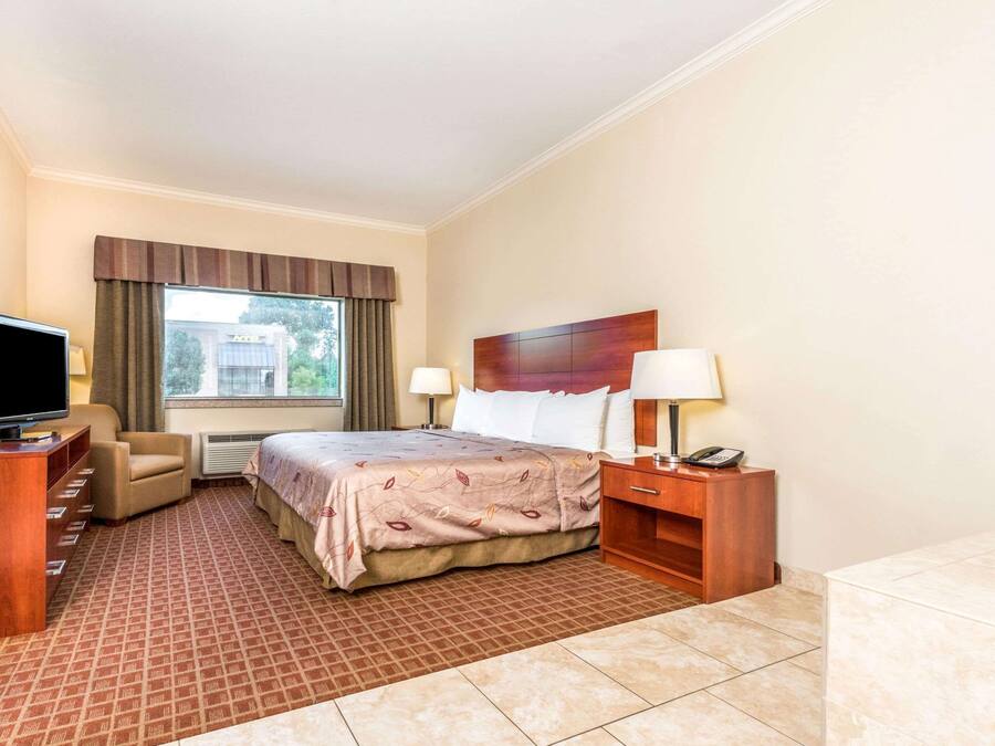 A hotel room with a bed, a TV, a desk, a chair, a lamp, and a telephone.