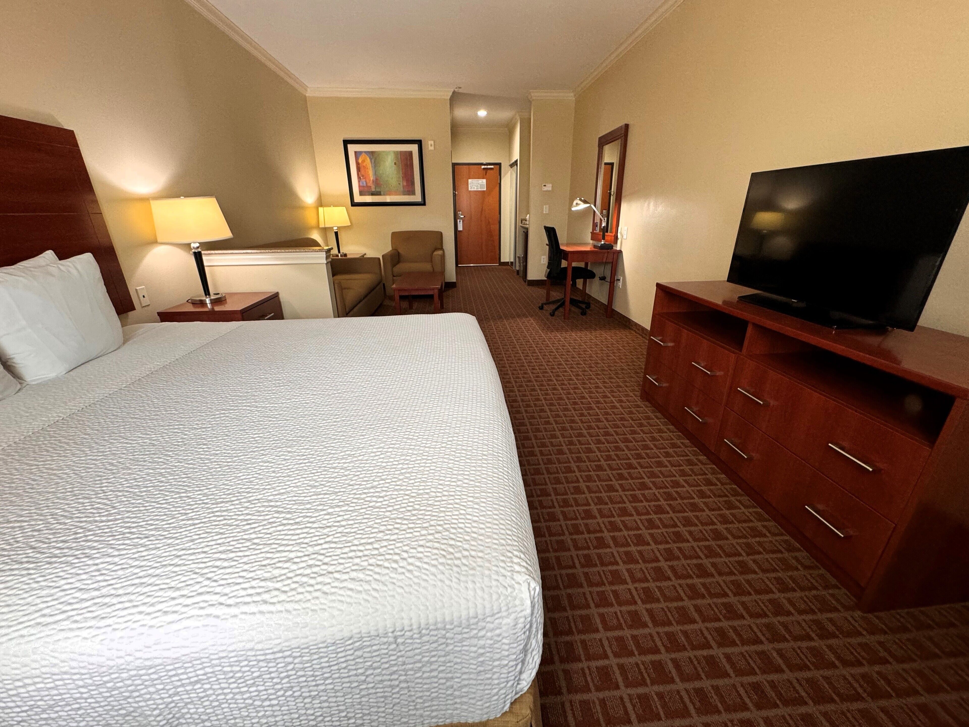 A hotel room with a large bed, a desk with a chair, a television, and a small table with a lamp.