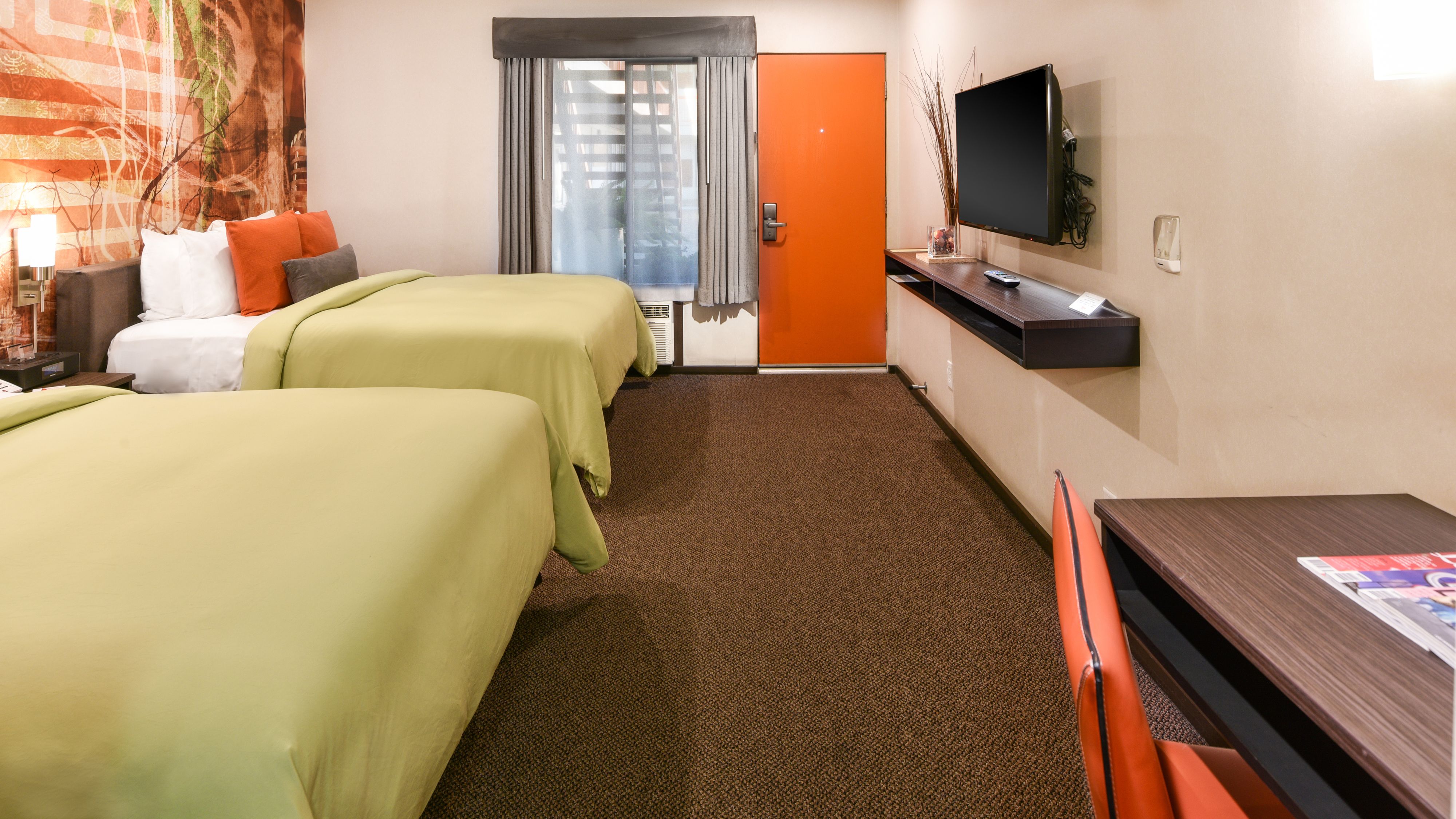 A hotel room with two beds, a TV, a desk, and a window with curtains.