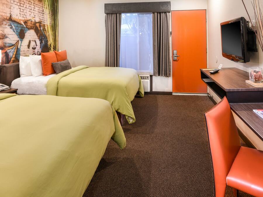 A hotel room with two beds, a desk, a TV, and a window with curtains.