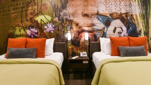 A hotel room with two beds, each with orange and grey pillows, and a wall mural. - The Tangerine - A Burbank Hotel (Burbank)
