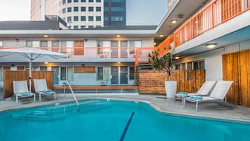 Un hotel moderno con piscina en la azotea, mobiliario exterior y vistas al perfil urbano de la ciudad.