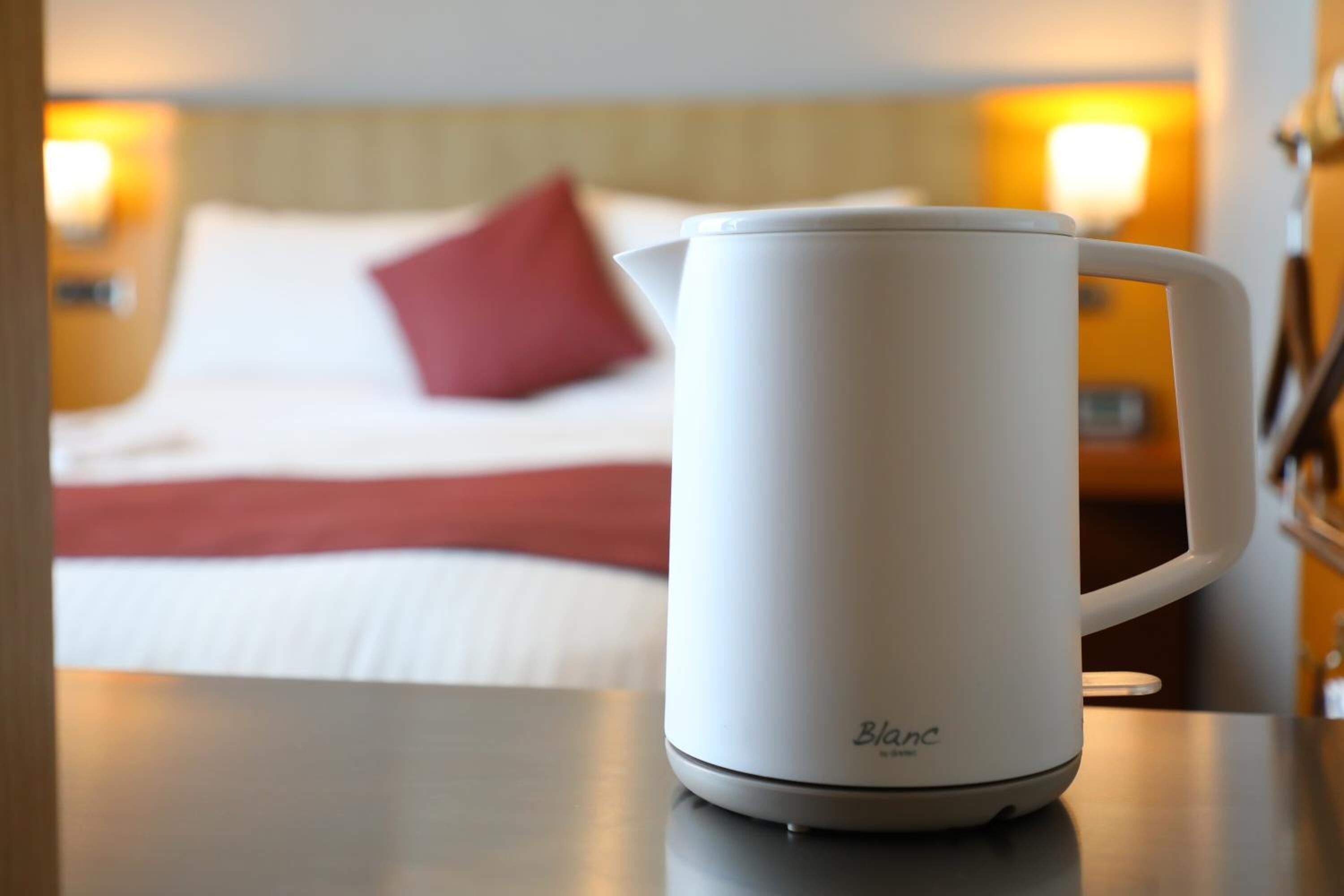 A white Blanc electric kettle on a table in a hotel room.