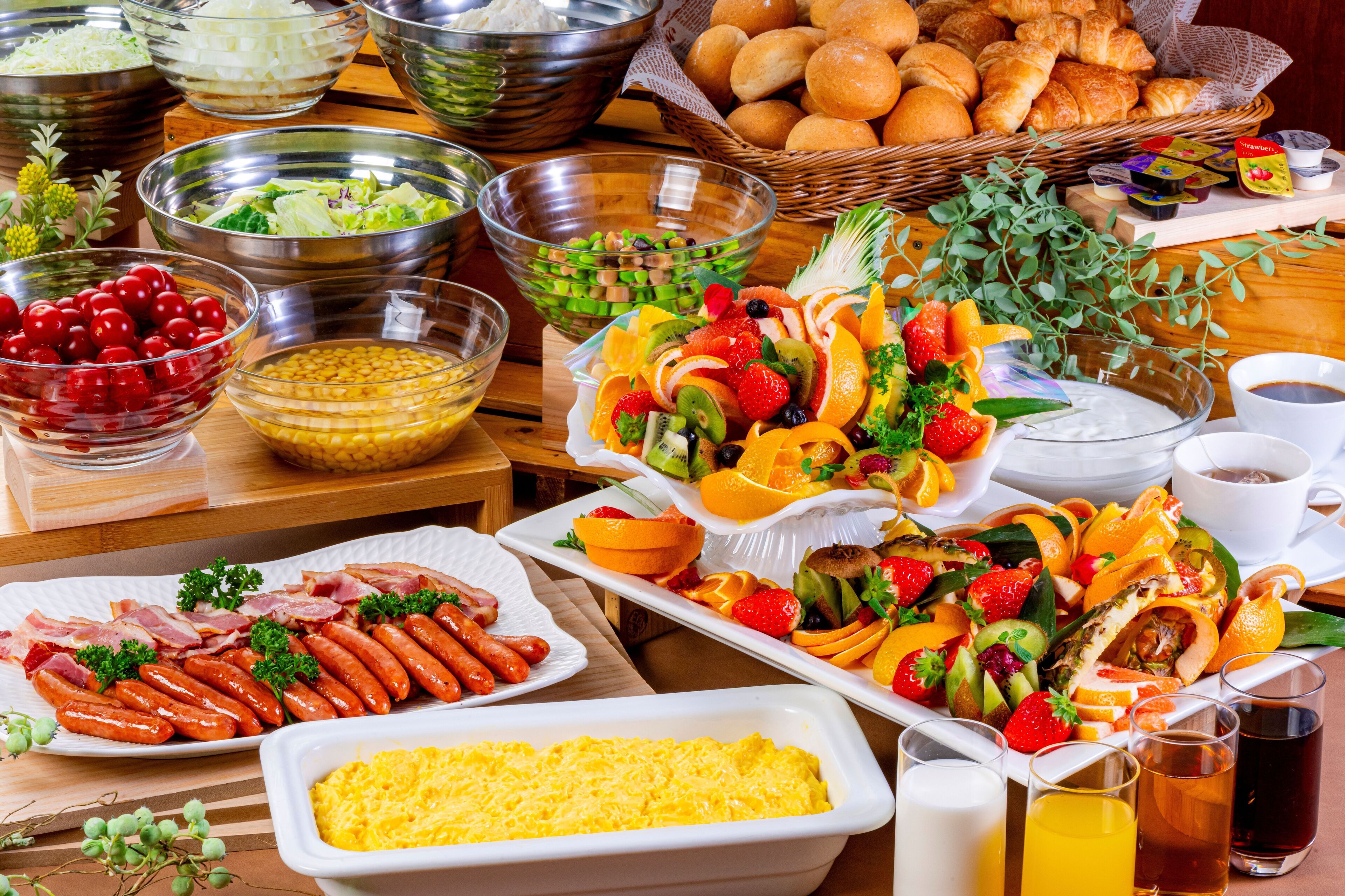 Buffet com diversos pratos, incluindo salsichas, saladas e uma seleção de frutas.
