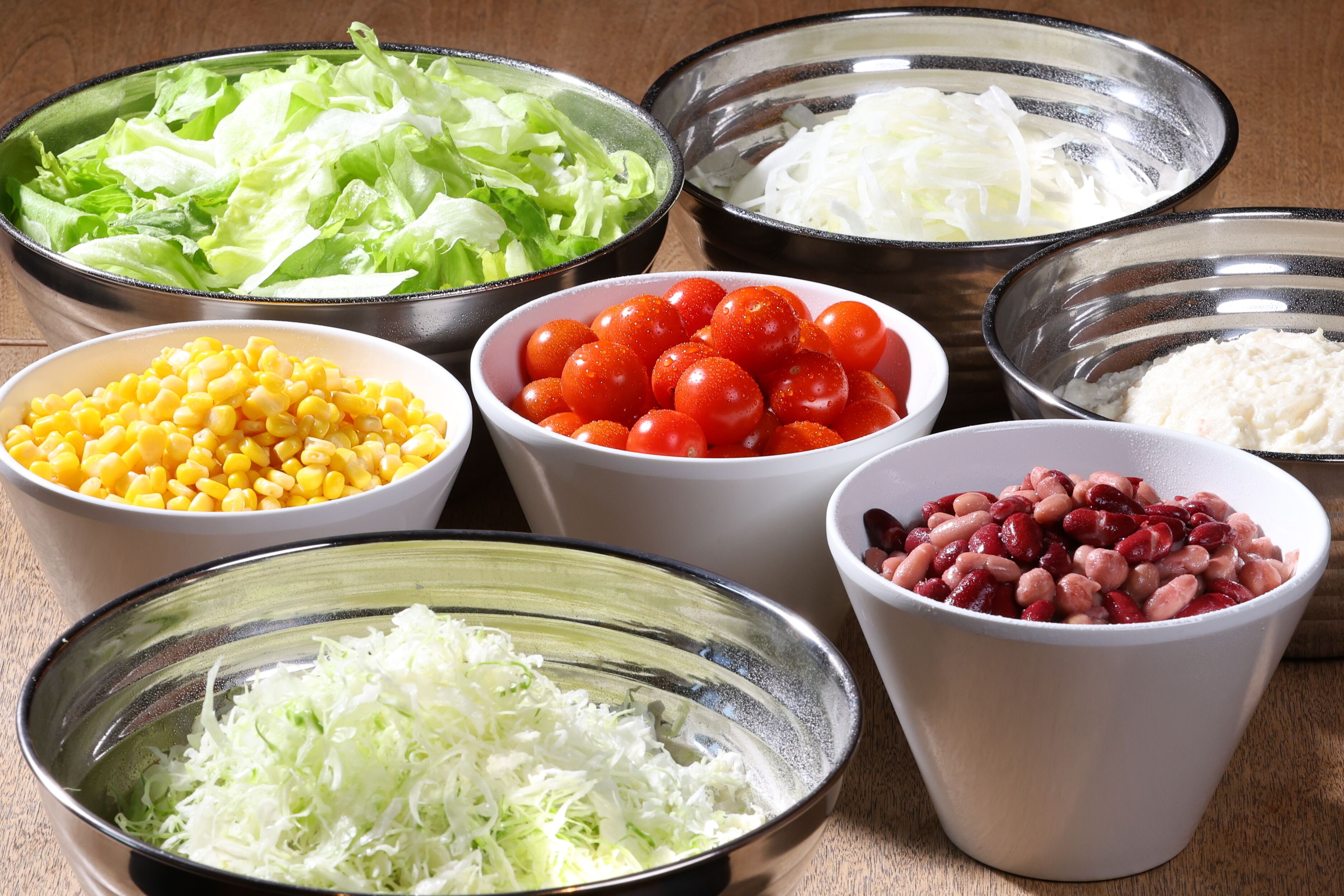 Tigelas com diversos ingredientes, incluindo alface, milho, tomate e feijão.