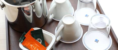 A tray with a stainless steel pot, white cups, a small dish with tea packets, and a glass container.