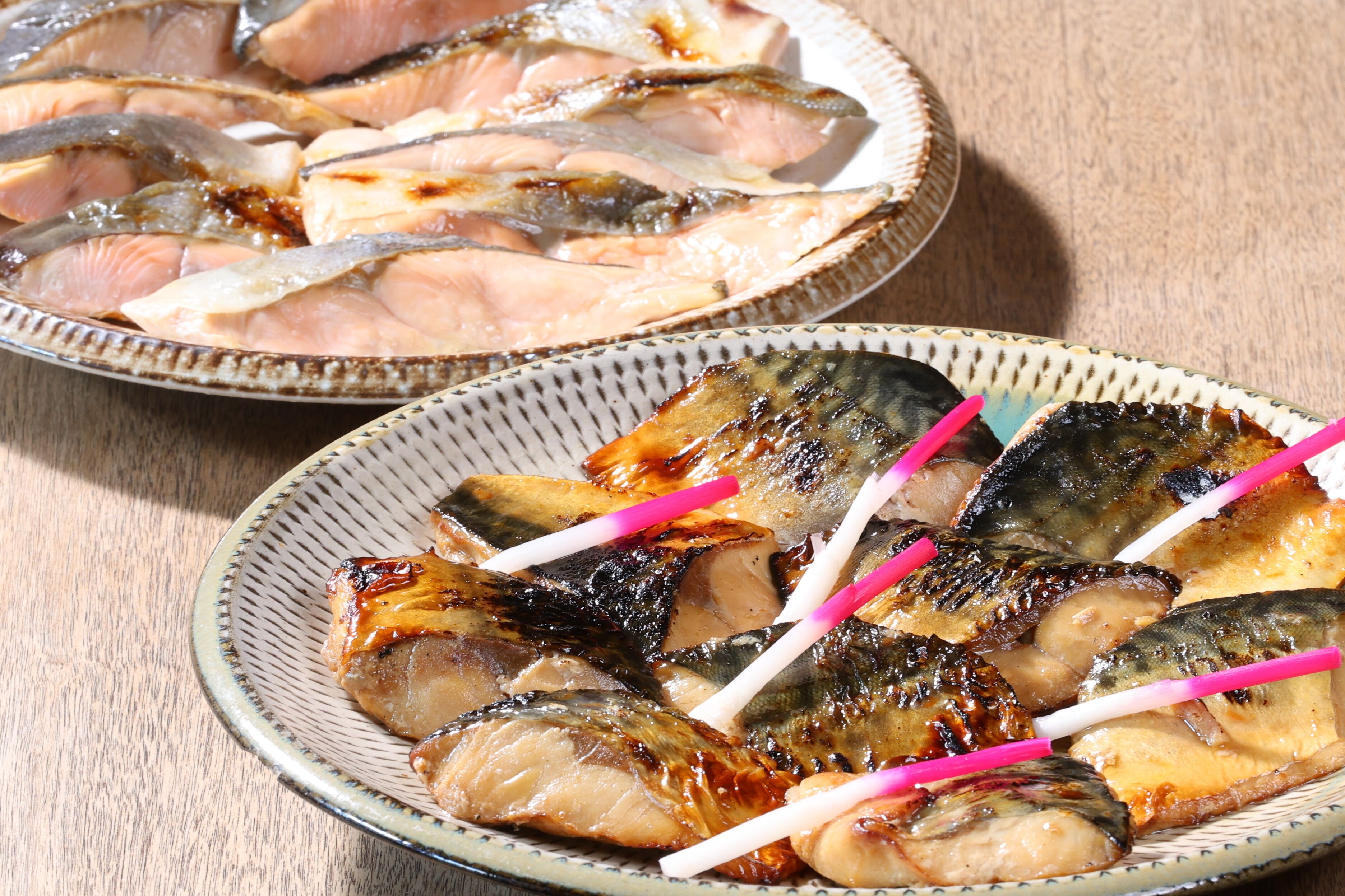 Two plates of grilled fish with pink pickled ginger sticks.