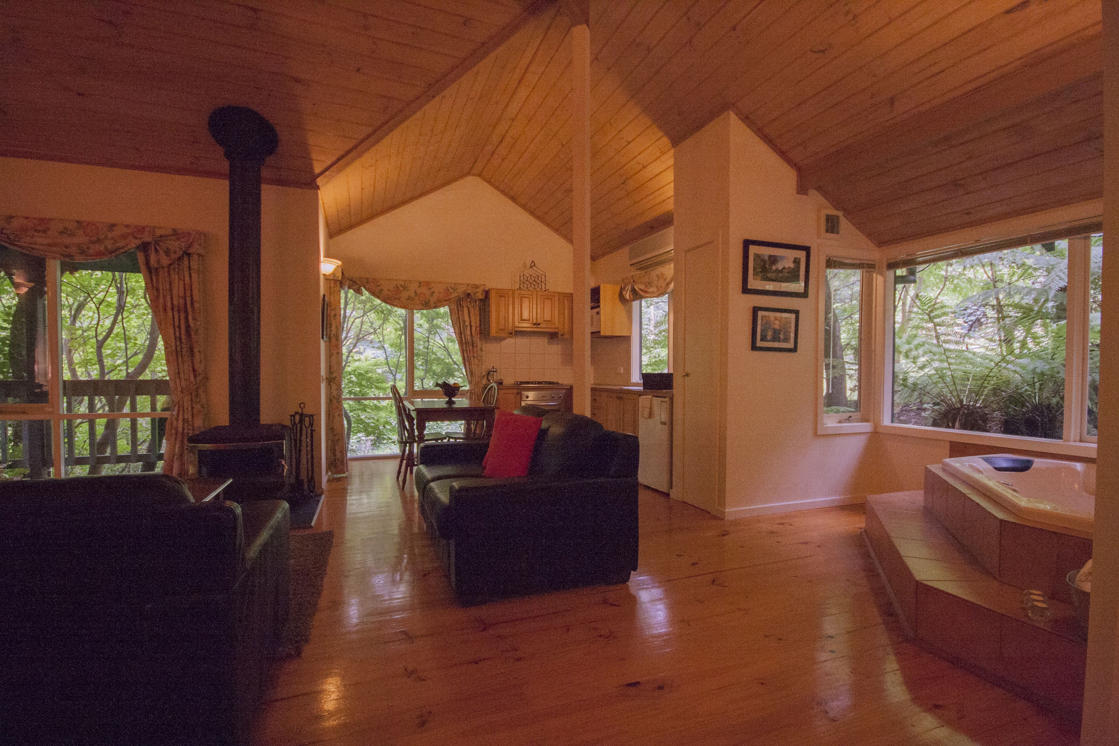 A spacious living area with a wooden ceiling, a fireplace, a dining area, and large windows offering a view of the outdoors.