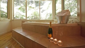 A room with a bathtub, a bottle of champagne, and three lit candles on a wooden bench. - Cottages at Monreale (Olinda)