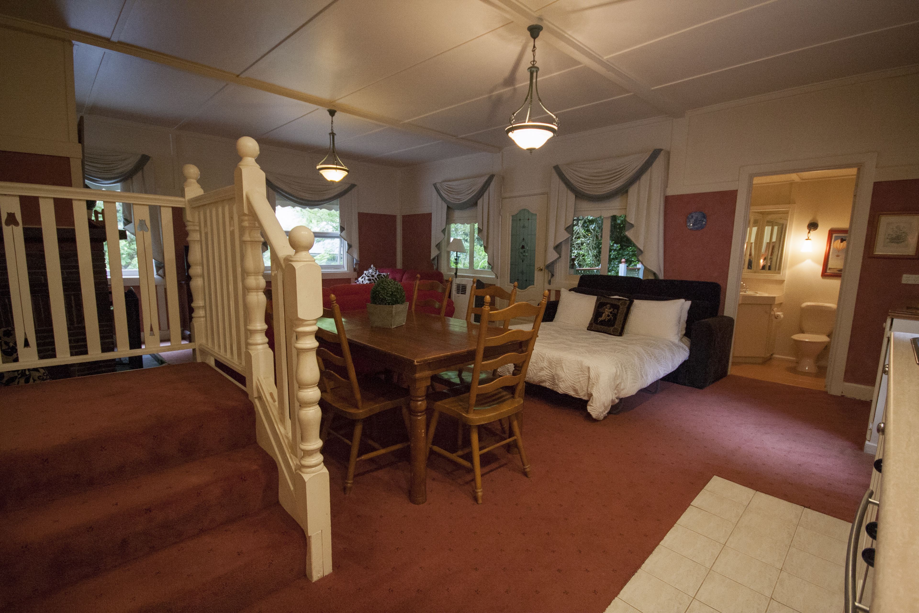 A room with a dining table, chairs, a bed, and a staircase.