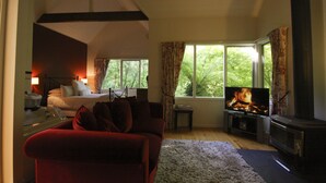 A modern living room with a sofa, a TV, a fireplace, and a bed with a nightstand. - Cottages at Monreale (Olinda)