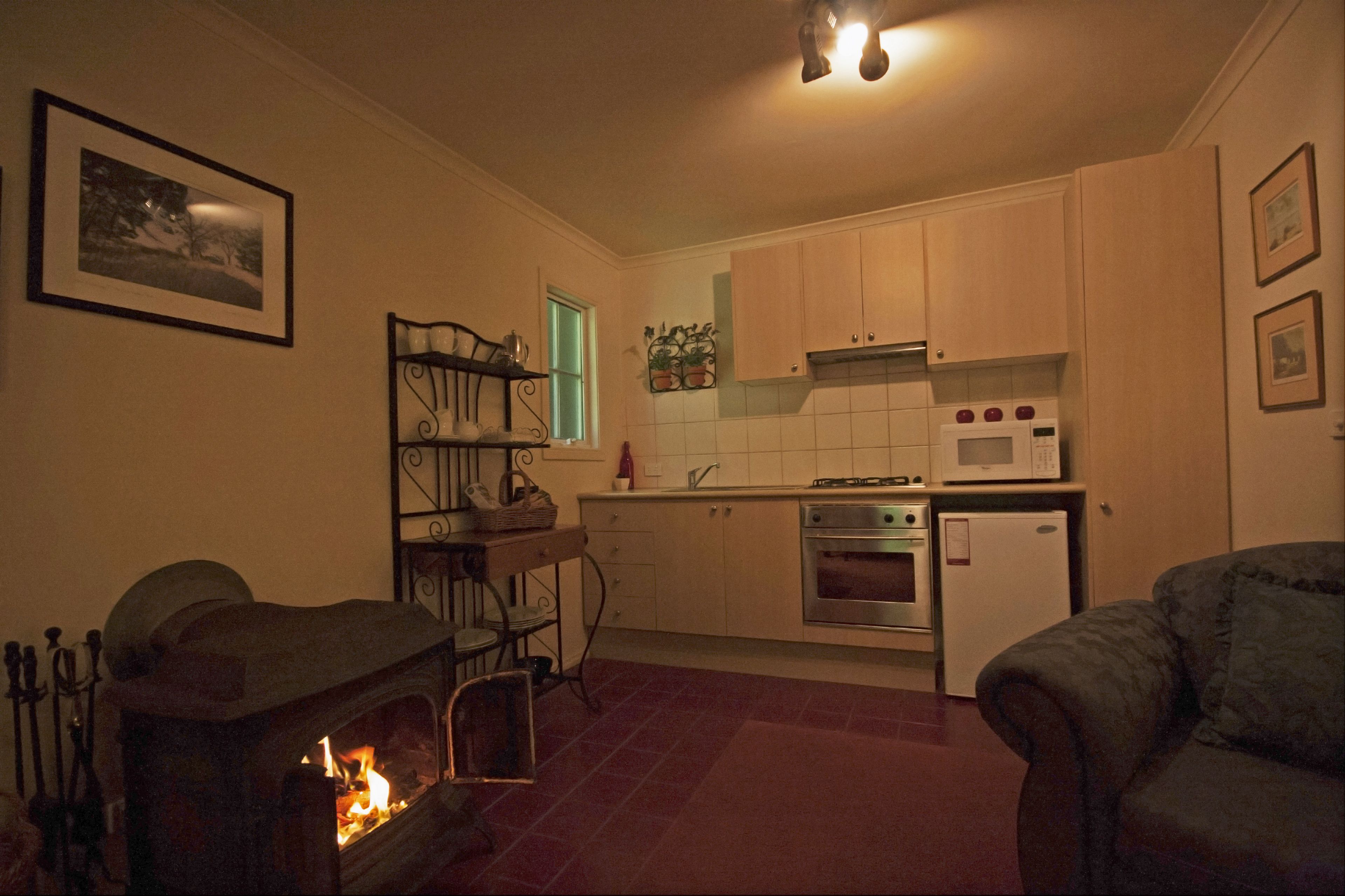 A cozy kitchen with a fireplace, wooden cabinets, a microwave, and a refrigerator.
