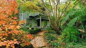 A green house with a porch, surrounded by autumn foliage and a stone pathway. - Cottages at Monreale (Olinda)