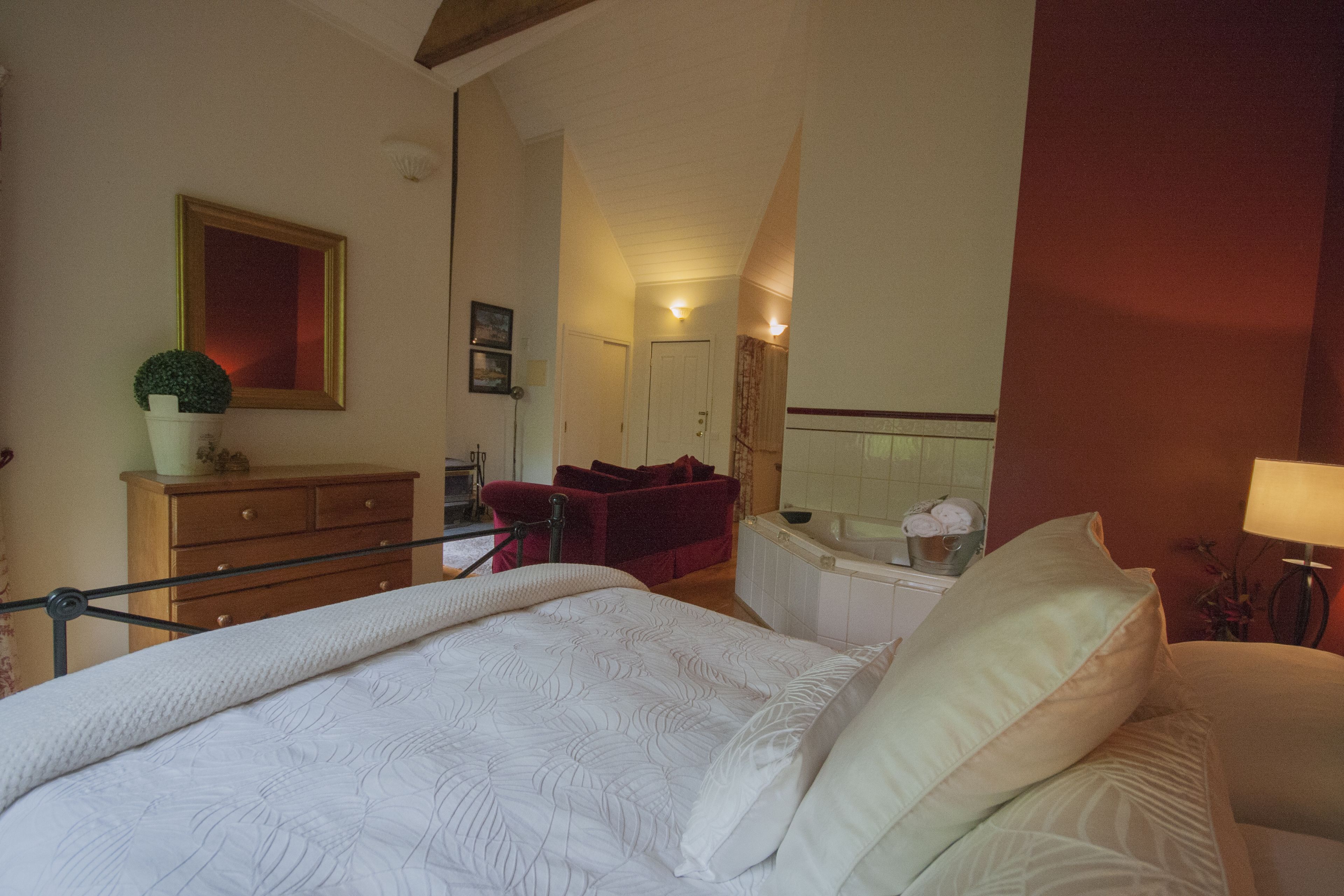Un dormitorio con cama, cómoda, silla roja, mesita con lámpara y baño con bañera.
