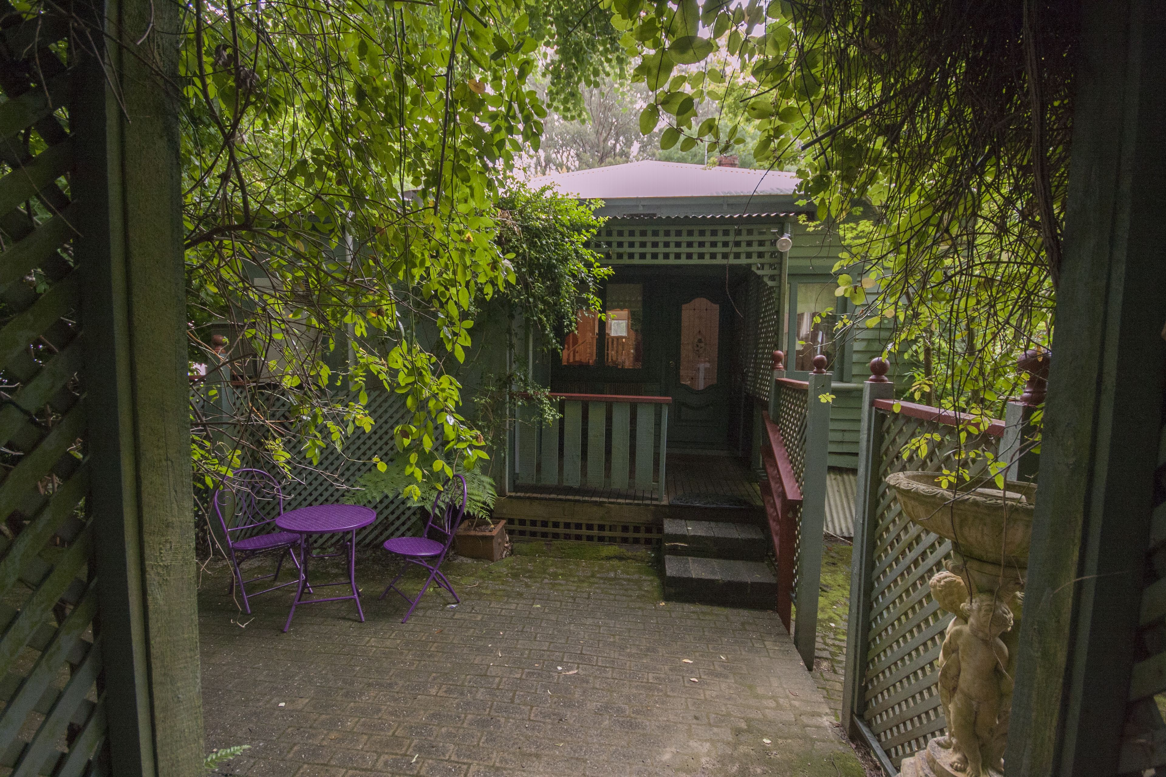 A covered outdoor seating area with a table and chairs, a small wooden structure, and a statue.